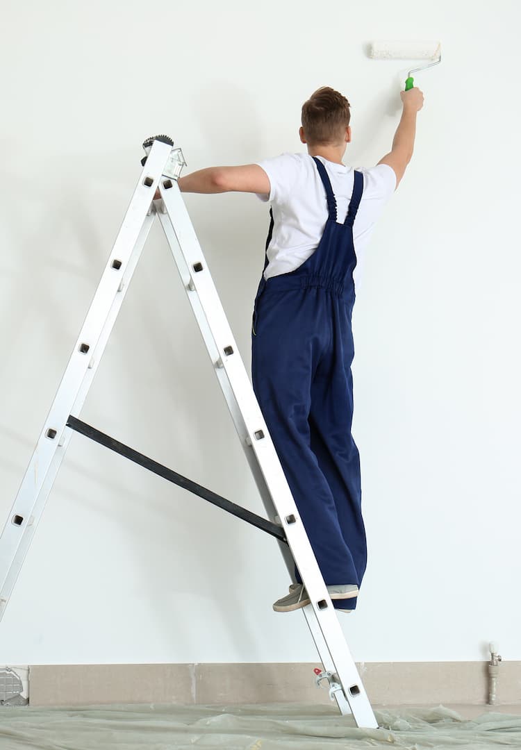 a man on a ladder painting a white wall