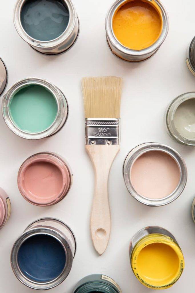 painting brush surrounded by pots of brightly coloured paint